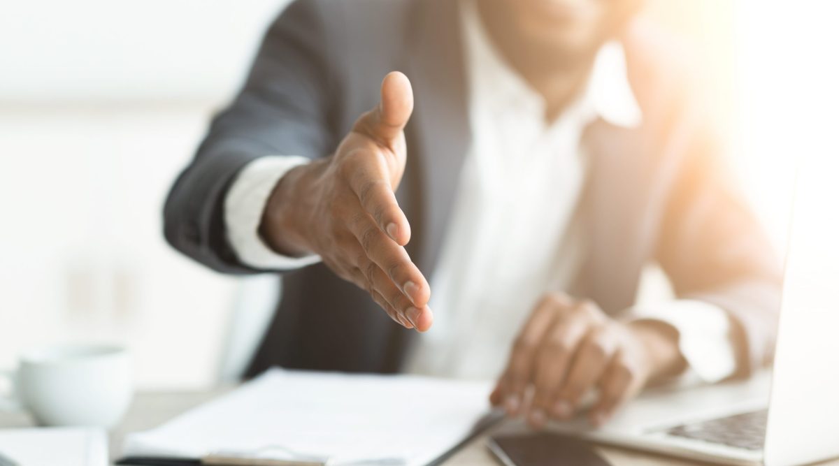 Black businessman giving hand for handshake on camera.